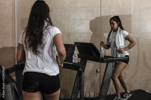 Mujer joven entrenado en la cinta de correr en el gimnasio con camiseta blanca y pantalón corto negro photo