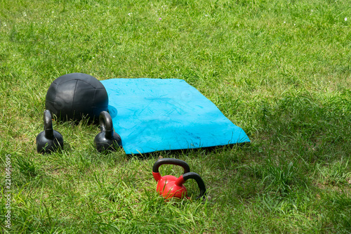 Bunch of fitness training weights on green grass background. Crossfit fitness equipment: medicine ball, few kettlebells, blue mat. Outdoor CrossFit Gym. Crossfit workouts outside photo