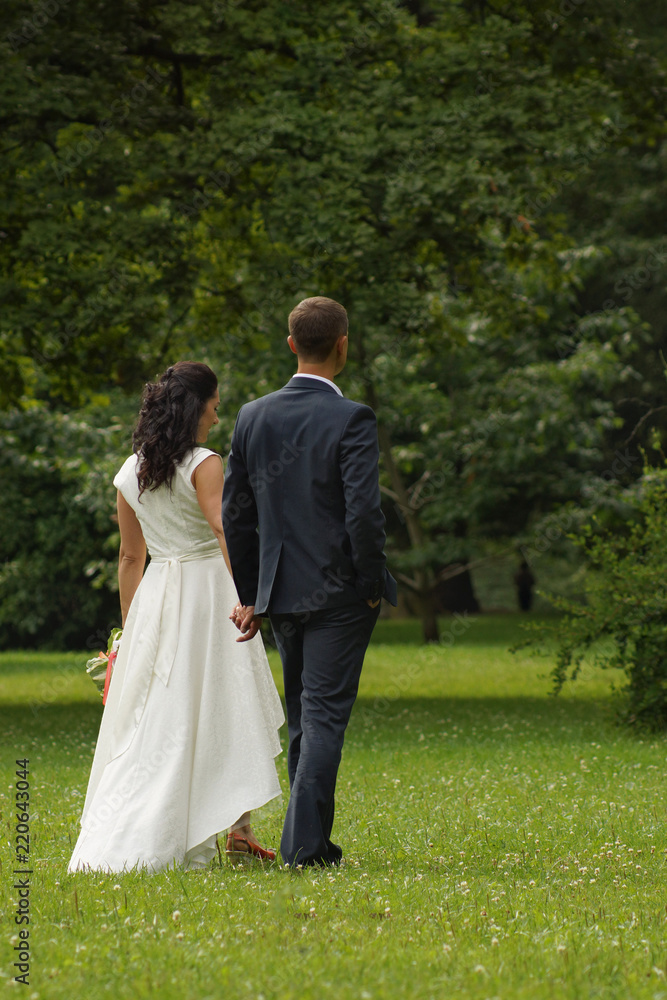 Two newlyweds standing in the park holding hands
