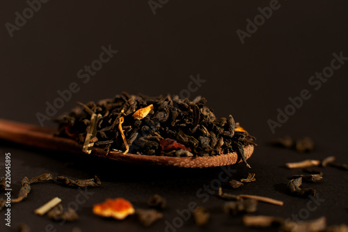 Tea leaves on a wooden spoon. Macro. Tea leaves on a black background. Isolate. Spoon with tea leaves close-up.