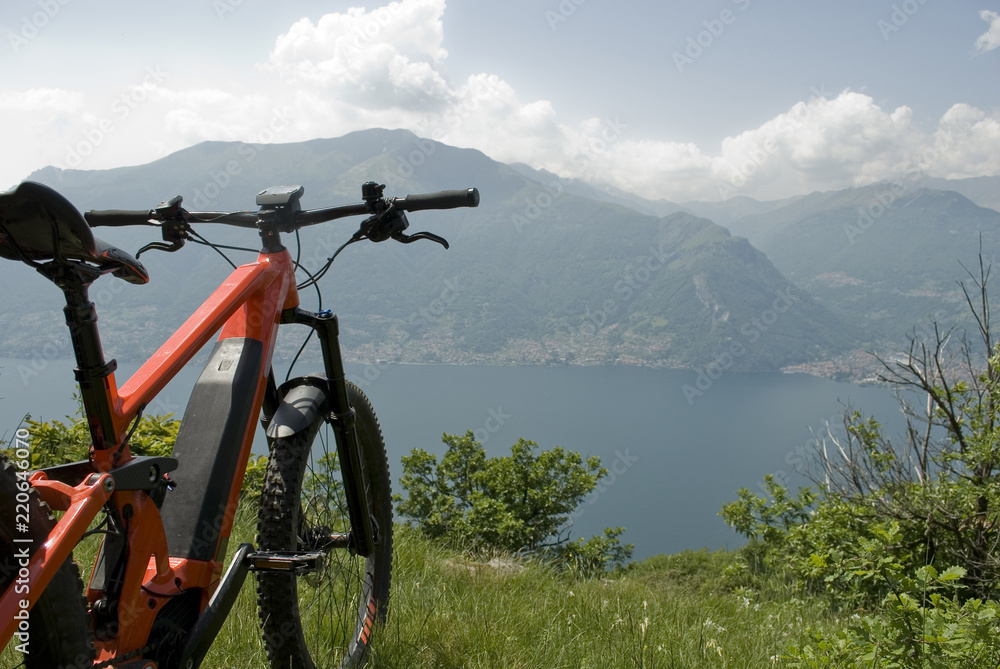 detail of electric bicycle, e-bike, ebike (handlebar, wheels, display), high mountains, valley, lake of Como, forest, summer, sport, adventure, freedom, sun, technology, holiday, alps, Lombardy, Italy