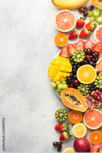 Colorfult raw fruits berries  mango  oranges  kiwi strawberries  blueberries grapefruit grapes  bananas apples on white plate  on off white table  top view  copy space  vertical