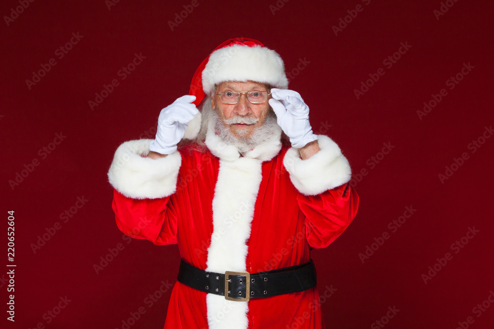 Christmas. Serious Santa Claus in white gloves adjusts her glasses and stares into the camera. Isolated on red background. Christmas. Serious Santa Claus in white gloves adjusts her glasses and stares into the camera. Isolated on red background.
