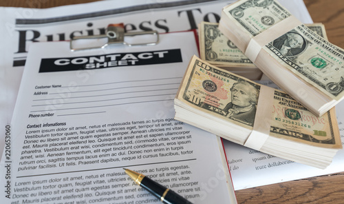 Businessmen are signing contracts document, with money as compensation, on wooden table.