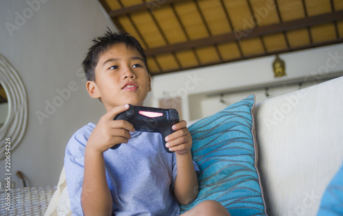  Latin young kid 8 years old excited and happy playing video game online holding remote controller enjoying having fun on couch in child gaming addiction