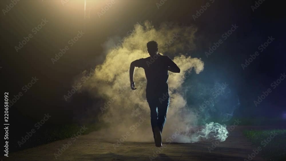 The man running in the cloud of smoke on the dark background, slow motion