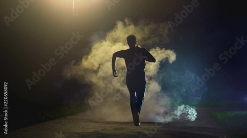 The man running in the cloud of smoke on the dark background, slow motion photo