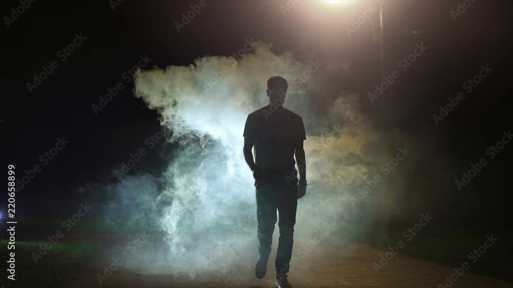 The man walking near the cloud of smoke on the dark background, slow motion The man walking near the cloud of smoke on the dark background, slow motion