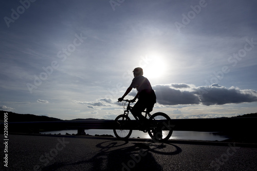 Fototapeta Naklejka Na Ścianę i Meble -  A silhouette of a cyclist with sunlit sky as background