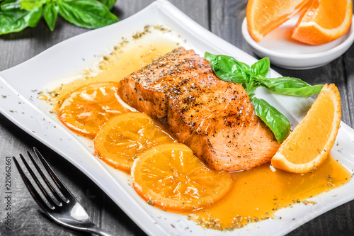 Photographie Honey Glazed fillet salmon with orange slices, spices and basil on white plate on dark background