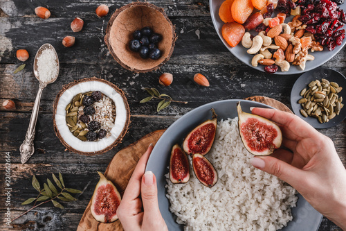 Woman cooking Rice coconut porridge with figs, berries, nuts and coconut milk in plate on rustic wooden background