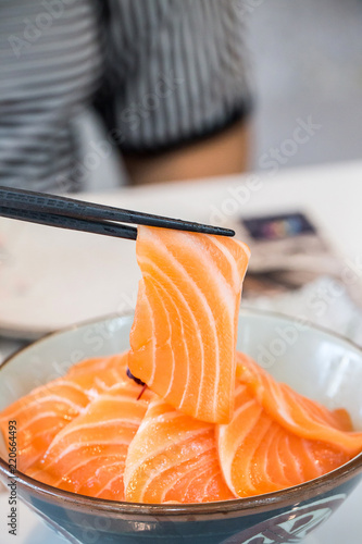 Close up salmon slice took by chopsticks. salmon topped by fresh salmon served with wasabi and soy sauce, donburi rice. image for background, copy space, decorate and menu list.