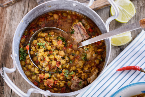 Delicious country soup from a mixture of legumes in a plate next to aluminum saucepan with soup is ready to be eaten for lunch