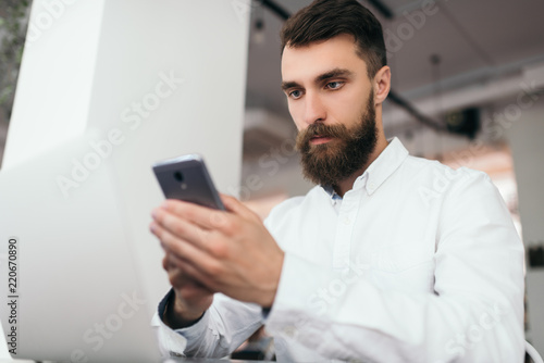 Bearded businessman using laptop computer and smartphone for project sitting in office space. Successful business. Attractive marketer write digital marketing plan, blog post and press release online.