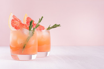 Summer cold cocktail with ice cubes, juice and slices grapefruit on pastel pink background.