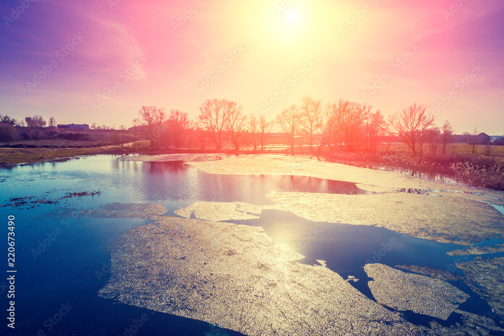 View of a river with floating ice in early spring at sunset. Rural landscape.