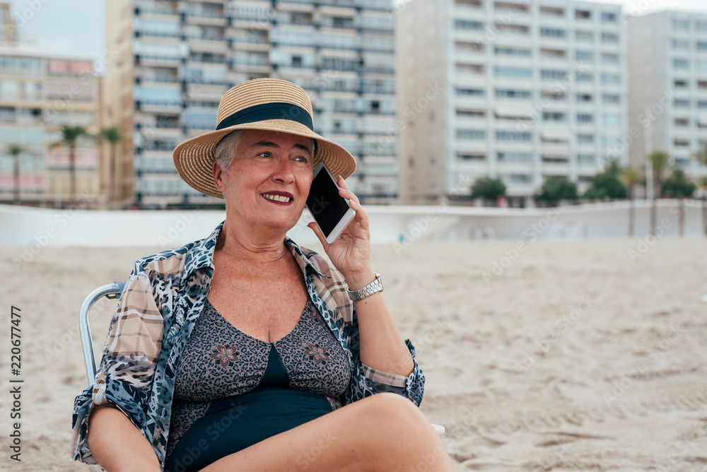 Elderly woman at the beach on the mobile phone