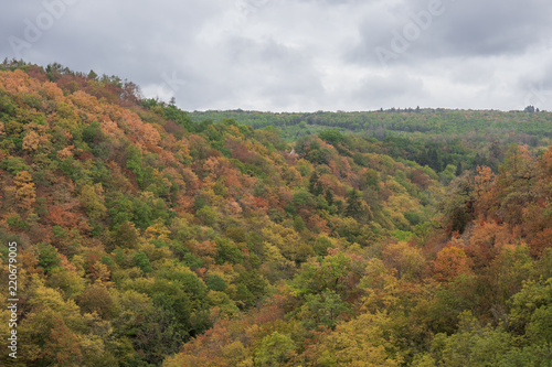European countryside landscape, hills covered by forest with the narrow valley in the middle. Early autumn stormy weather, sky with dark clouds, colorful trees.