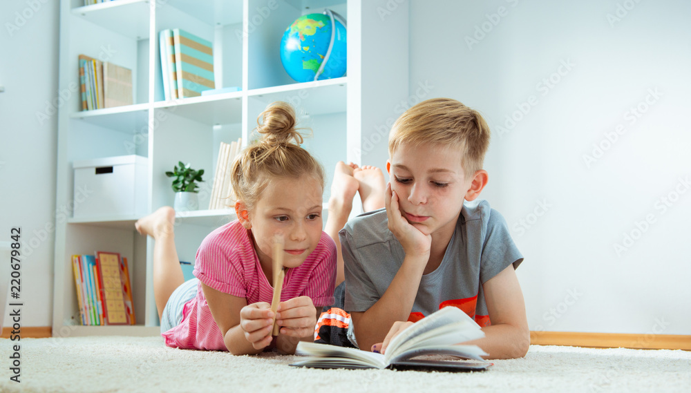 Portrait of two children reading a book on the floor at home Portrait of two children reading a book on the floor at home
