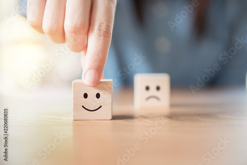 Close up customer hand choose smiley face and blurred sad face icon on wood cube, Service rating, satisfaction concept.