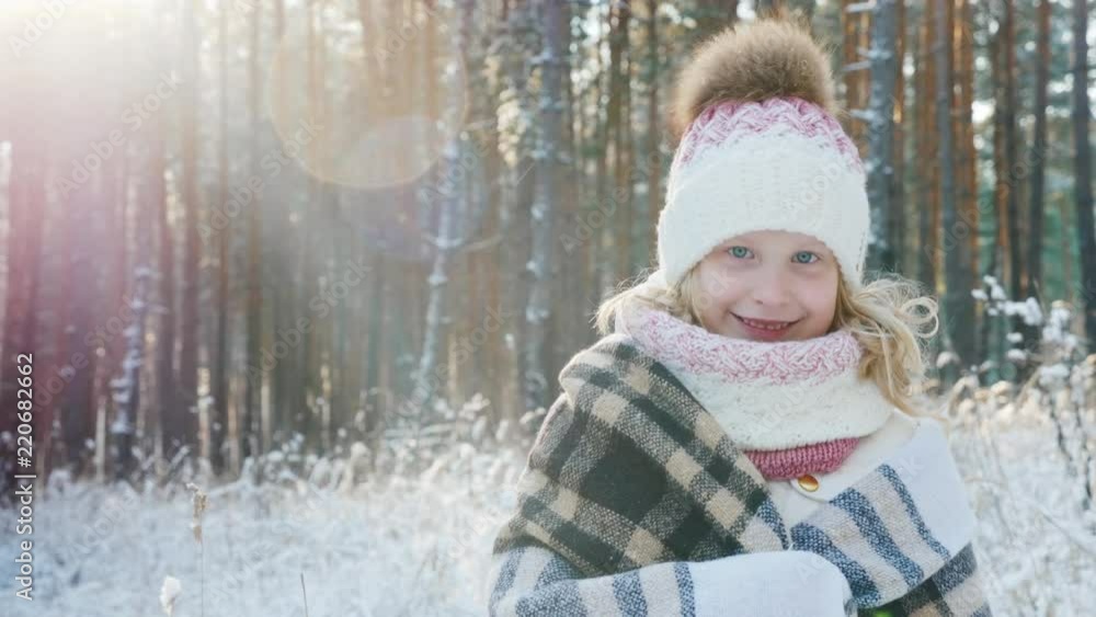 Portrait of a happy little girl wrapped in a plaid in a snow-covered winter forest Portrait of a happy little girl wrapped in a plaid in a snow-covered winter forest