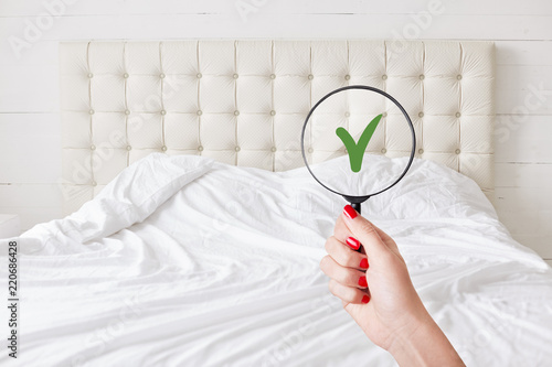 Everything in perfect and clean. Woman checks condition in hotel room, holds lens against white bed which demonstrates purity and tidiness. Whiteness concept