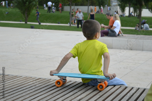 Мальчик со скейтом сидит на лавке в городском парке.