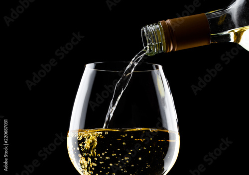 Pouring white wine from bottle to glass on black