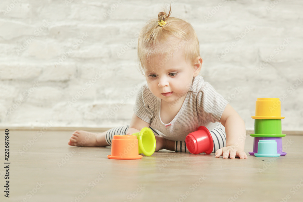 Baby girl playing on the floor with plastic educational cups, early learning concept Baby girl playing on the floor with plastic educational cups, early learning concept