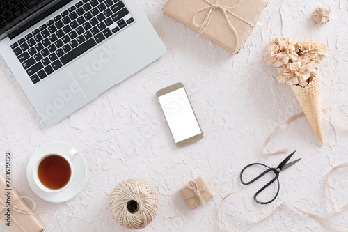 Top view of woman workspace with laptop, beige flowers, smartphone on white textural background, flat lay. Stylish female blogger concept.