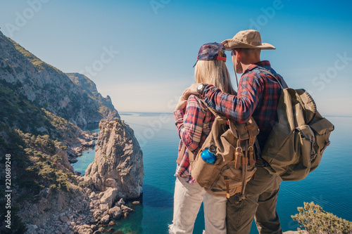 Man and woman backpackers standing and hugging on the mountain. Couple hikers with backpacks relaxing on top of a hill and enjoying sea view and cliffs. photo
