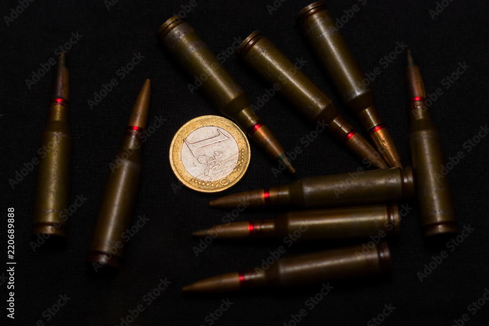 Rifle ammo around one euro coin on black background. Symbolizes the war for money and one of the world's problems. Rifle ammo around one euro coin on black background. Symbolizes the war for money and one of the world's problems.