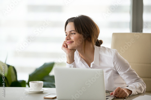 Happy businesswoman looking away satisfied with good new job enjoying business success and wellbeing working in office, smiling woman boss feeling motivated dreaming thinking about future goals