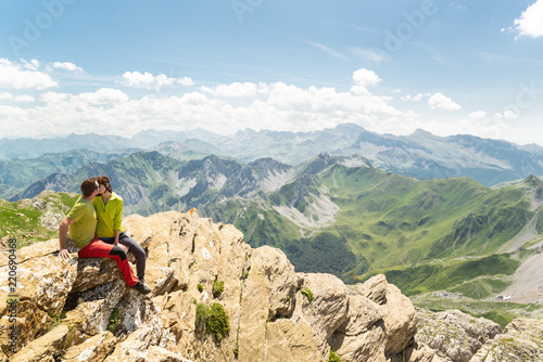 Joven pareja besándose en la cima de una montaña rodeada de un hermoso paisaje. Amor y vacaciones de aventura.