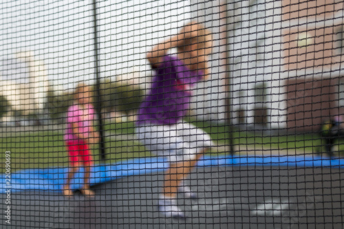 Defocused background of children on a trampoline. Grid in the foreground. Child Safety Concept © Laura Сrazy