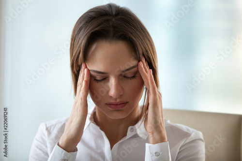 Chronic headache concept, young exhausted woman suffers from migraine touching temples to relieve pain, tired fatigued lady feels dizzy of overwork, stress or hormonal imbalance, headshot, front view