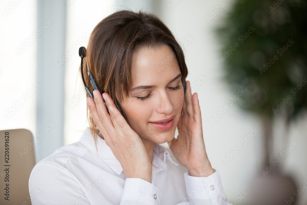 Young woman in headphones enjoying pleasure from good music for relaxation, smiling lady wearing headset listening to new favorite audio tracks podcast during office break to reduce work stress Young woman in headphones enjoying pleasure from good music for relaxation, smiling lady wearing headset listening to new favorite audio tracks podcast during office break to reduce work stress