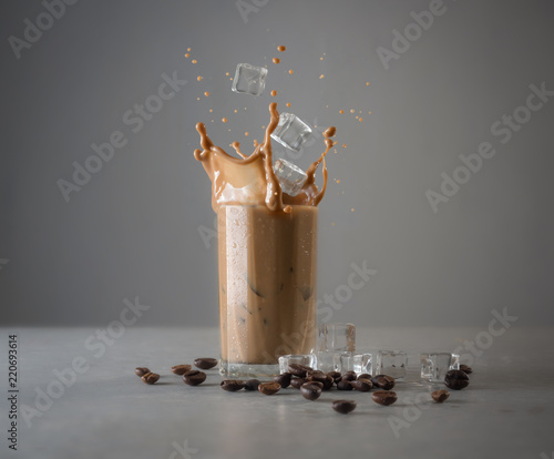 Iced coffee splash with ice cubes and beans against grey concrete