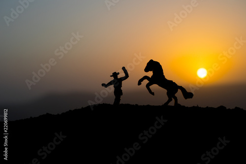 Fototapeta Naklejka Na Ścianę i Meble -  Cowboy concept. Silhouette of Cowboys at sunset time. A cowboy silhouette on a mountain with an yellow sky.