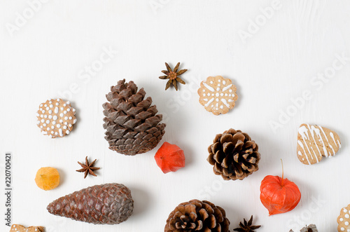 Bright top view Christmas layout with gingerbread cookies, pine cones and orange physalis on a white wooden surface.