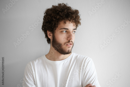 Close up shot of attractive stylish young unshaven man with fuzzy beard and voluminous hair having serious look, posing at white blank studio wall. Human facial expressions, emotions and feelings © Anatoliy Karlyuk