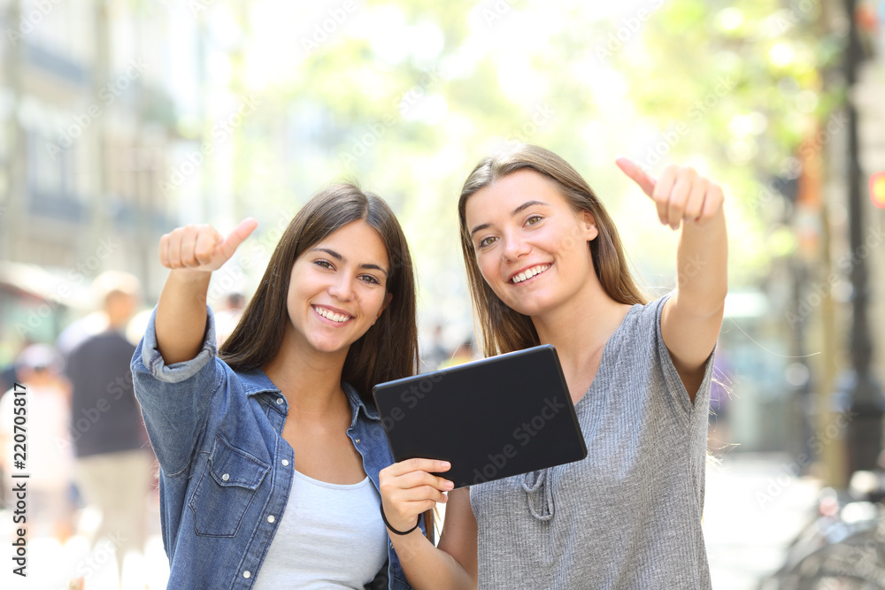 Happy friends holding a tablet with thumbs up Happy friends holding a tablet with thumbs up