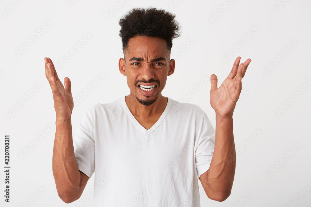Closeup of angry african american young man with curly hair and raised hands wears t shirt feels irritated and arguing isolated over white background Closeup of angry african american young man with curly hair and raised hands wears t shirt feels irritated and arguing isolated over white background