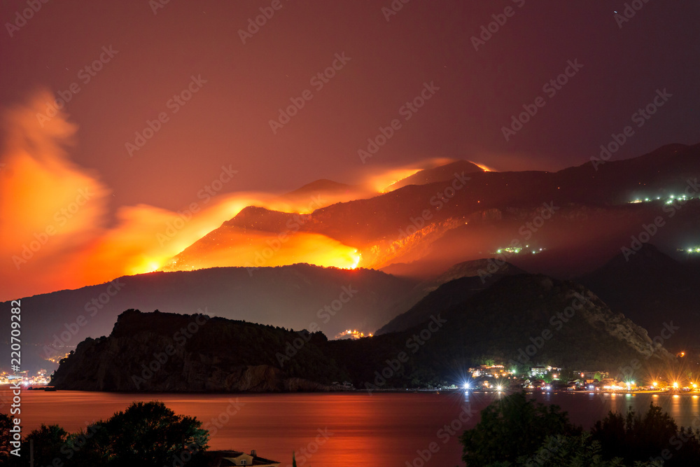 Wild fire blazing on hills above sea town.