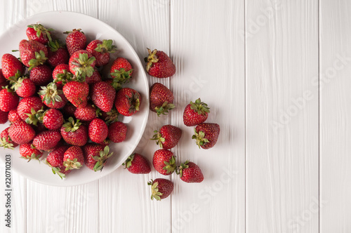 Fresh strawberries in a plate on a white wooden background.