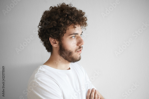 Close portrait of attractive young Caucasian male with curly hair, thick beard and beautiful features posing isolated in studio with blank copy space wall for your text or promotional information © Anatoliy Karlyuk