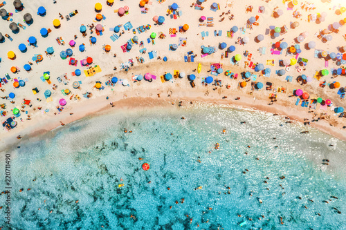 Aerial view of sandy beach with colorful umbrellas, swimming people in sea bay with transparent blue water at sunset in summer. Travel in Mallorca, Balearic islands, Spain. Top view. Landscape