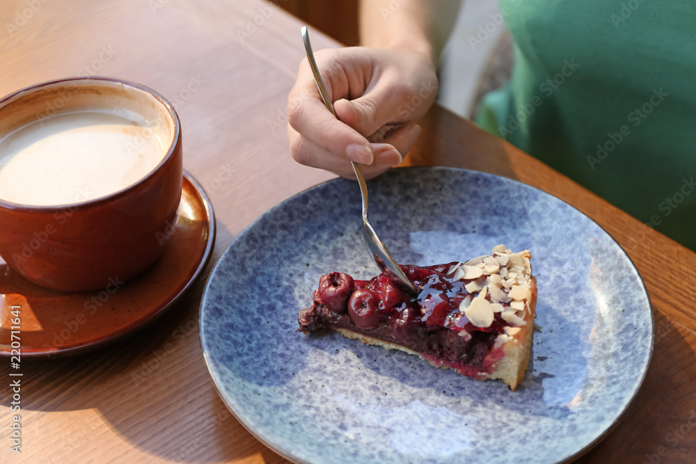 Woman eating slice of cherry cake at table, closeup