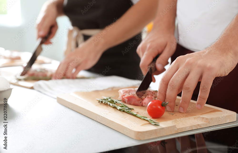 Male chef cutting meat on wooden board at table, closeup