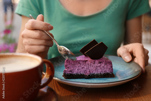 Woman eating slice of berry cheesecake at table, closeup